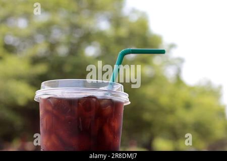 Verschließen Sie den Eiskaffee in einer Plastiktasse. Paket zum Mitnehmen und einfach zu erfrischen. Mit Gartenblick und Bokeh-Hintergrund. Stockfoto