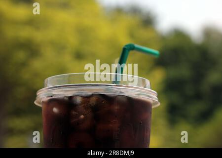 Verschließen Sie den Eiskaffee in einer Plastiktasse. Paket zum Mitnehmen und einfach zu erfrischen. Mit Gartenblick und Bokeh-Hintergrund. Stockfoto