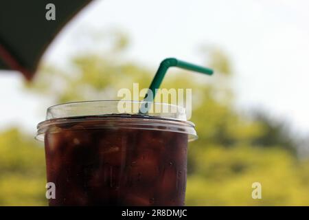 Verschließen Sie den Eiskaffee in einer Plastiktasse. Paket zum Mitnehmen und einfach zu erfrischen. Mit Gartenblick und Bokeh-Hintergrund. Stockfoto