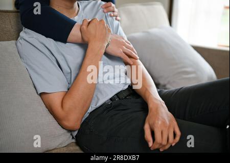 Zugeschnittenes Bild eines glücklichen schwulen Paares, das sich umarmt, während er sich einen Film auf einem Fernseher auf einer Couch im Wohnzimmer ansieht. Sorgenfrei und glücklich Stockfoto