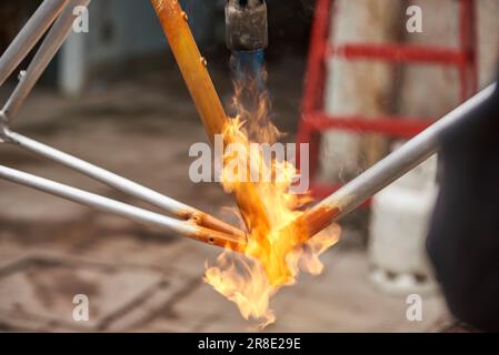 Manuelle Fahrradrenovierungsarbeiten, Lackentfernung durch Brennerfeuer, um die Farbe eines Fahrradrahmens zu ändern. Nahaufnahmen ohne Leute. Stockfoto