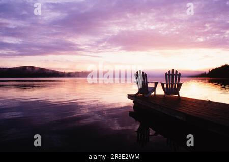 USA, New York State, Saranac Lake, Silhouettes of adirondack Stühle am Pier am Lake Placid bei Sonnenaufgang im Adirondack Park Stockfoto