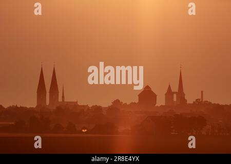 Halberstadt, Deutschland. 21. Juni 2023. Das Licht der Morgensonne kämpft sich durch eine Wolkenschicht über dem Vorharz-Gebirge bei Halberstadt während der Sommersonnenwende. Die Türme der Halberstädter Kathedrale (L.) und St. Martin's Church ist im Hintergrund zu sehen. Am astronomischen Beginn des Sommers kann es bis zu 17 Stunden Sonnenschein geben. Es ist der längste Tag des Jahres. Kredit: Matthias Bein/dpa/Alamy Live News Stockfoto