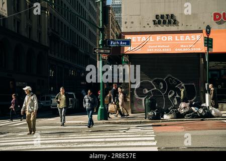 Geschäftige Straßenszene in New York City mit Gruppen von Personen, die über eine überfüllte Kreuzung auf der Fifth Avenue in Midtown Manhattan, NYC, laufen. Hohe Qualität Stockfoto