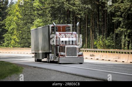 Brauner industrieller Großlaster klassischer amerikanischer Idol-Sattelschlepper, der kommerzielle Fracht in einem glitzernden Sattelanhänger transportiert, der sich auf dem Highway Roa bewegt Stockfoto