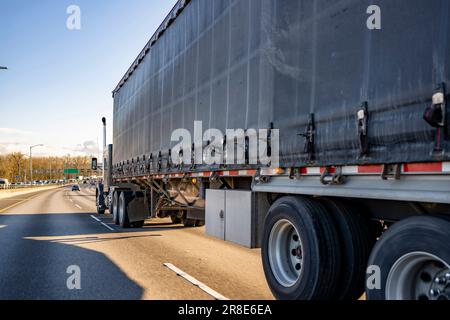 Schwarzer industrieller Sattelschlepper mit Motorhaube und hohem Fahrerhausfach für Lkw-Fahrer, der kommerzielle Fracht in einem trockenen Van auf Auflieger transportiert Stockfoto