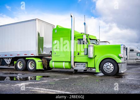 Grüner, großer Lkw-Sattelzugmaschine mit amerikanischer Motorhaube und erweitertem Fahrerhausfach für Lkw-Fahrerplatz und Anhänger/Auflieger mit trockenem Lieferwagen, der auf dem steht Stockfoto