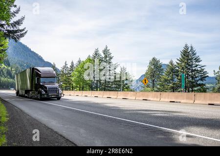 Brauner industrieller Großlaster klassischer amerikanischer Idol-Sattelschlepper, der kommerzielle Fracht in einem glitzernden Sattelanhänger transportiert, der sich auf dem Highway Roa bewegt Stockfoto