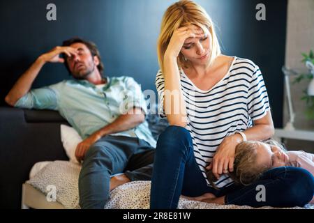 Müde Mutter und Vater, die auf der Couch sitzen, fühlen sich genervt, erschöpft, stressig mit dem kleinen Mädchen. Stockfoto