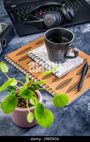 Von zu Hause aus arbeiten. Schreibtisch mit Laptop, Notizblock, Kaffeetasse, Kopfhörern und Pflanze Stockfoto