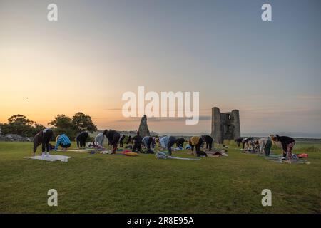 Hadleigh Castle, Großbritannien. Juni 2023. Während eines Sonnenaufgangs im Hadleigh Castle, Essex, können die Teilnehmer morgens auf Yogamatten posieren. Die Ruinen und die Steinsilhouette vor dem frühen Licht erinnern an antike Rhythmen und saisonale Erneuerung. Ein ruhiger, gemeinschaftlicher Moment, der Erbe, Wellness und Natur miteinander verbindet. Eine Gruppe übt Yoga, während die Sonne zur Sommersonnenwende an den Ruinen der Burg in der Stadt aufgeht. Penelope Barritt/Alamy Live News Stockfoto
