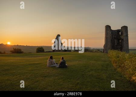 Hadleigh Castle, Großbritannien. Juni 2023. Zwei Personen sitzen bei Sonnenaufgang auf einer Decke neben den Ruinen von Hadleigh Castle in Essex, England, und beobachten den Sonnenaufgang zur Sommersonnenwende. Das goldene Licht taucht das alte Mauerwerk und das Grasfeld auf und erinnert an Themen der saisonalen Erneuerung, der historischen Kontinuität und der ruhigen Feier. Penelope Barritt/Alamy Live News Stockfoto