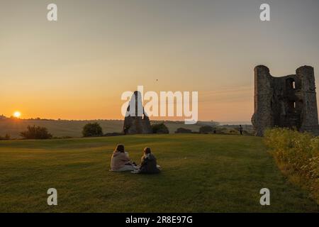 Hadleigh Castle, Großbritannien. Juni 2023. Zwei Personen sitzen bei Sonnenaufgang auf einer Decke neben den Ruinen von Hadleigh Castle in Essex, England, und beobachten den Sonnenaufgang zur Sommersonnenwende. Das goldene Licht taucht das alte Mauerwerk und das Grasfeld auf und erinnert an Themen der saisonalen Erneuerung, der historischen Kontinuität und der ruhigen Feier. Penelope Barritt/Alamy Live News Stockfoto