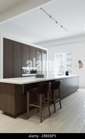 Minimalismus in der Küche. Holzküche mit großer langer Insel und Barhockern. Stockfoto