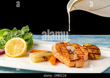 Gegrillter Lachs in Sauce mit Gemüse und Kartoffeln auf einem weißen Porzellanteller Stockfoto