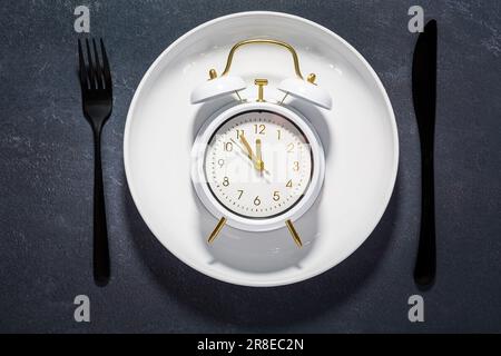 Weiße Platte und Uhr auf dunklem Hintergrund mit Kopierbereich. Konzept von Intervallnüchtern und Autophagie. Stockfoto