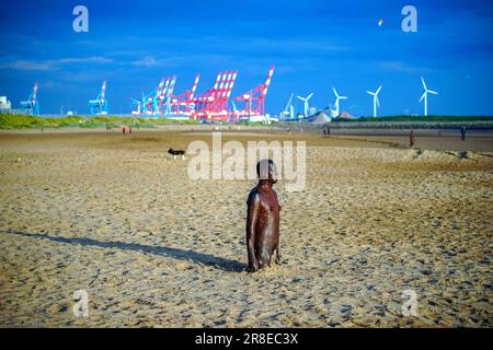 Menschen genießen das warme Wetter an einem anderen Ort, Anthony Gormleys Ironmen Statuen am Crosby Beach, Merseyside, am Vorabend der Sommersonnenwende. Foto: Dienstag, 20. Juni 2023. Stockfoto