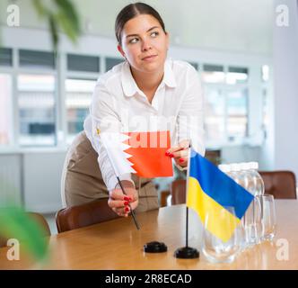 Koordinatorin des Büros, die die Flaggen der Ukraine und Bahrains auf den Verhandlungstisch setzt Stockfoto