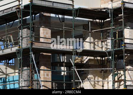 Ein Außenbereich eines neuen zweistöckigen Hauses im Bau mit einer geschäftigen, überladenen Montage von Gerüsten, Mauerwerk, Metallrahmen und -Paneelen Stockfoto