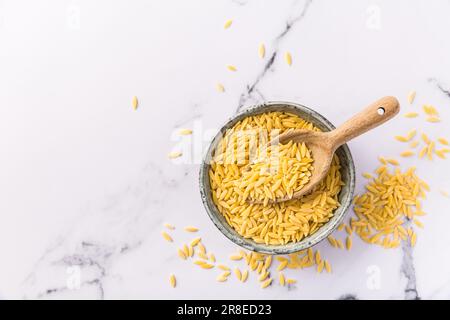 Rohe Orzo-Pasta (Risoni) in Schüssel mit Holzlöffel Stockfoto