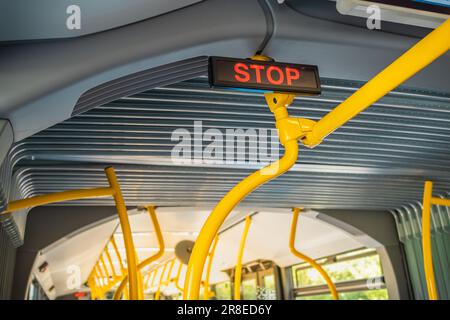 Stoppschild im Stadtbus. Leere Bushaltestelle. Bus mit blauen Sitzen und gelben Handläufen Stockfoto