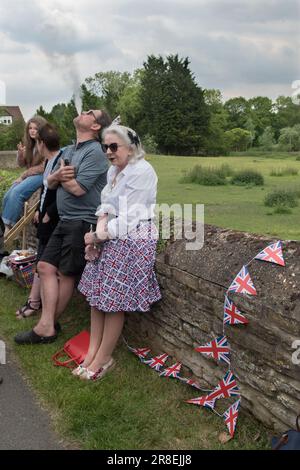 Verdampfender E- Zigarettenmann bläst Rauch weg UK. Queen Elizabeth II Platin Jubiläum Straßenfest Feiern. Ein Mann "raucht" eine elektronische Zigarette. Statt Rauch atmet der Benutzer Dampf ein. Mit einer E-Zigarette wird er oft als „Vaping“ bezeichnet und bläst den Dampf weg. Viele Menschen trugen rot, weiß und blau die ältere Frau trägt einen Union Jack Flaggenrock. Lowick, Northamptonshire, England, 3. Juni 2022. HOMER SYKES Stockfoto