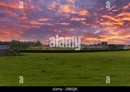 Blick über grüne Felder bei Sonnenuntergang in Richtung der Stadt Dreghorn in der Ferne an einem hellen Frühlingstag im Mai mit zwei neu errichteten Siegern Stockfoto