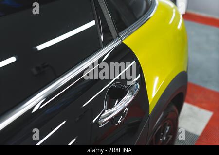 Fahrzeugverpackungskonzept. Nahaufnahme einer speziellen Vinylfolie in Limettengelb auf der Oberfläche eines modernen schwarzen Autos. Hochwertiges Foto Stockfoto