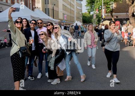 Platinum Jubilee Street Party. Die Kings Road, Chelsea zum Teil für den Verkehr gesperrt, die Menschenmassen von Einheimischen und Touristen genießen das Sommerwetter. Junge, wohlhabende Erwachsene, treffen sich in einer Gruppe und lächeln für die Kamera. Sie machen ein Selfie mit einem Smartphone. Dunkle Brillen sind in Mode. London, England 4. Juni 2022. HOMER SYKES Stockfoto