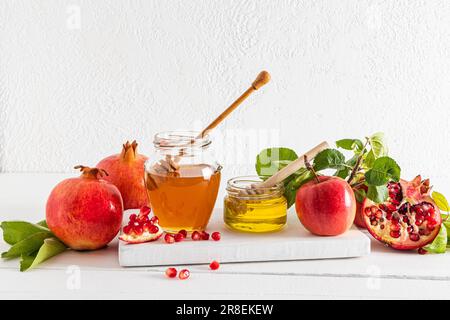 Vorderansicht von zwei Dosen Honig, reife Granatäpfel und Äpfel auf einem weißen Holzpodiumbrett. Traditionelles Neujahrsgeschenk für Roshashan Stockfoto