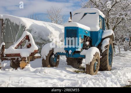 Der alte Traktor liegt im Schnee, bedeckt von einem Bauernhof Stockfoto