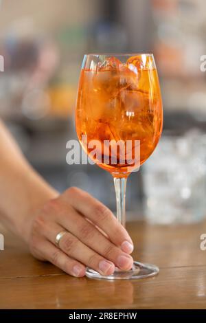 Roter Cocktail aperol mit einer Scheibe Rüben in Glas in den Händen des Barkeepers an einer Bar Stockfoto