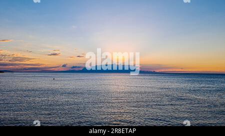 Bild des Sonnenaufgangs über dem Meer, versteckt von Wolken mit intensiven Farben und Sonnenstrahlen im Sommer Stockfoto