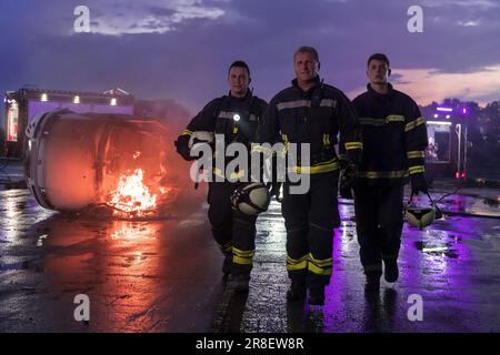 Das Team der tapferen Feuerwehrleute geht zur Kamera. Im Hintergrund Sanitäter und Feuerwehr Rettungsteam bekämpfen Feuer in Autounfall, Versicherung und Rettung von Menschen Stockfoto