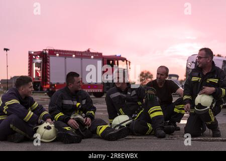 Das Team der tapferen Feuerwehrleute geht zur Kamera. Im Hintergrund Sanitäter und Feuerwehr Rettungsteam bekämpfen Feuer in Autounfall, Versicherung und Rettung von Menschen Stockfoto