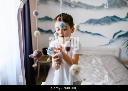 Der ältere Bruder spielt mit mobilen Spielzeugen für Neugeborene im schönen Kinderzimmer, glückliche Kindheit Stockfoto