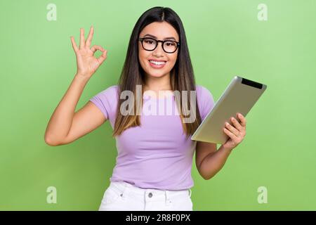 Foto einer hübschen jungen vietnamesischen chinesin-Lady-Hold-Tablet mit ekligen Details in elegantem violetten Kleidungsstück isoliert auf grünem Hintergrund Stockfoto