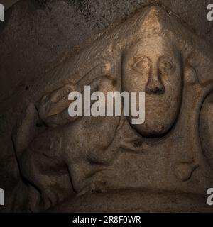 Das in Marmor geformte Gesicht blickt aus der romanischen Hauptstadt im Kreuzgang hervor, das in den späten 1200s Jahren der Abteikirche St. Michael oder der église abbatiale St-Michel in Saint-Génis-des Fontaines, Pyrénées-Orientales, Occitanie, Frankreich, hinzugefügt wurde. Stockfoto