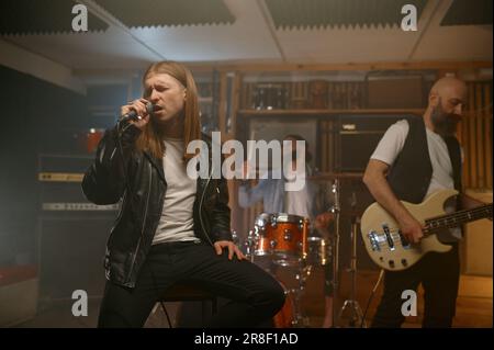 Geschlossene Aufführung einer Rockband mit Fokus auf jungen Sänger mit Mikrofon Stockfoto