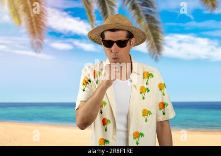 Ein lateinischer Mann im Urlaub trägt ein geblümtes Hemd, eine Sonnenbrille am tropischen Strand und fühlt sich unwohl und hustet als Symptom für Erkältung oder Bronchitis. Gesundheitswesen Stockfoto