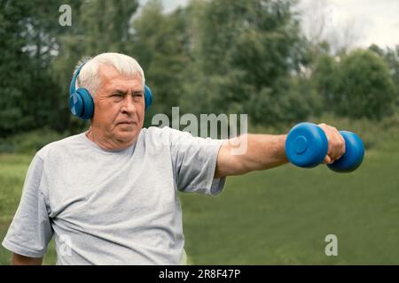 Senior-Mann, der draußen trainiert. Person, die Kurzhanteln hebt. Ein alter Mann, der im Park trainiert. Lebensstil gesunder Menschen. Aktives Sporttraining. Ältere Menschen Stockfoto
