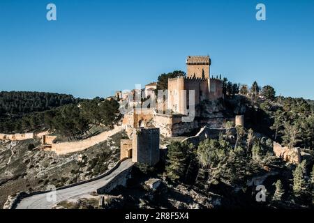 Diese majestätische Alarcon Festung, eine mittelalterliche Burg in Spanien, steht stolz auf einer hohen Klippe, umgeben von üppigen Bäumen Stockfoto