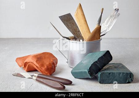 Eine Vielzahl von Werkzeugen zum Formen und Modellieren in einem Aluminiumbecher und Stücken Ton und Plastik auf einem leichten Steinhintergrund in einer Werkstatt Stockfoto