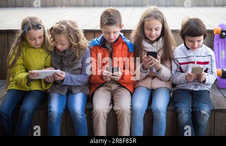 Mädchen und Jungen mit Smartphones auf der Bank im Herbst im Park Stockfoto