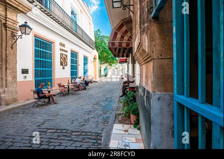 Leute an einem sonnigen Tag sitzen, essen, plaudern und genießen die Zeit in Havanna auf einer leeren Straße mit Tischen. Stockfoto