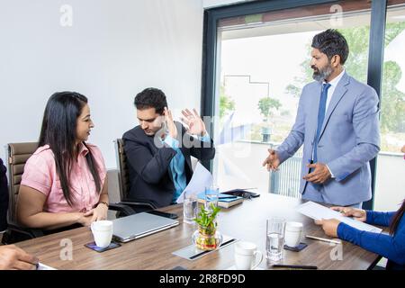 Wütender indischer Boss, der männliche Angestellte wegen schlechter Arbeit anschreit, Geschäftsmann-ceo, schimpft inkompetenten Manager, beschuldigt ihn und wirft ihm Papiere ins Gesicht für mi Stockfoto