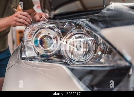 Autotönungsservice - Arbeiter-Spezialist trägt in der Werkstatt eine Farbfolie auf den Autoleuchten auf Stockfoto