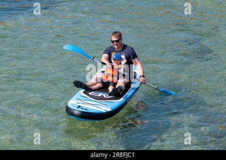 18. Juni 2023 Cullen, Moray, Schottland. Das ist ein Mann mit seinem Sohn auf einem Paddleboard, der die Sonne genießt, der Fotograf bekam eine Welle vom Sohn. Alle lächeln. Stockfoto