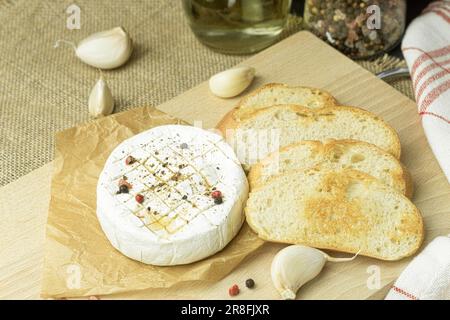 Nahaufnahme von französischem Camembert-Käse, der im Ofen gebacken werden kann. Serviert mit Croutons auf einem Holzbrett auf dunklem Holzhintergrund, Blick von oben Stockfoto