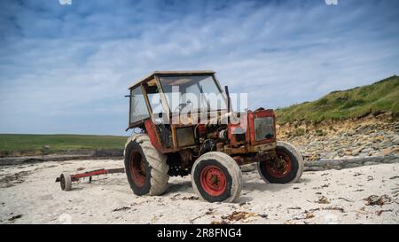 Der rostige alte Traktor hat kleine Fischerboote vor einem Strand in Orkney, Schottland, Großbritannien, geworfen. Stockfoto